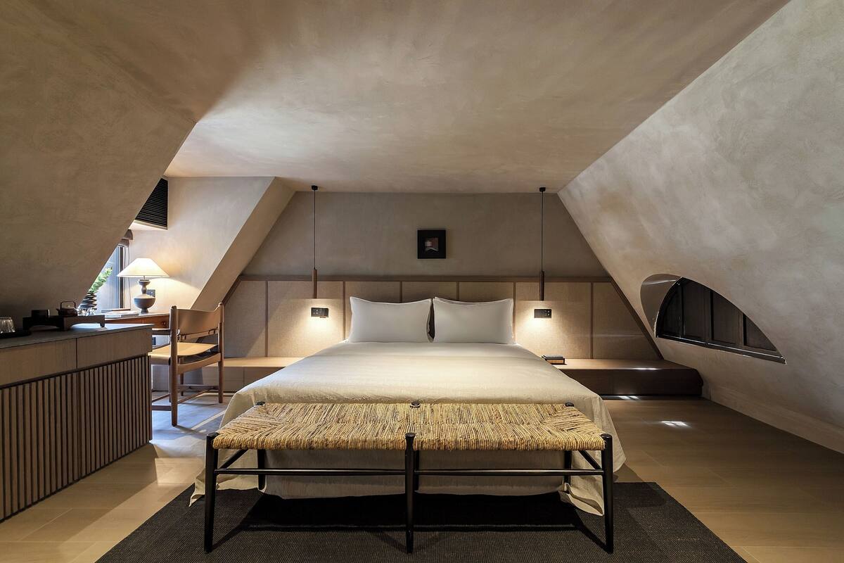 A modern bedroom with a large bed, bedside tables, a small desk, and a window.