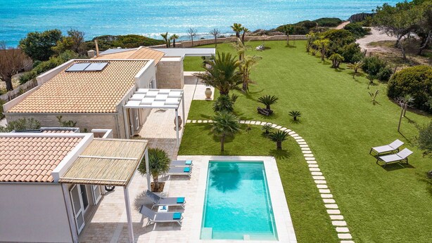 Area piscina sul tetto con vista libera sul mare, circondata da un prato curato e qualche palma.