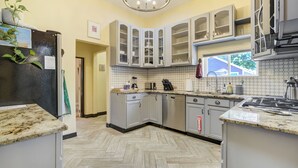 Une cuisine avec un sol en parquet disposé en point de Hongrie, des meubles blancs, un réfrigérateur en acier inoxydable et une cuisinière encastrée.