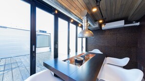 A modern dining area with a long table, white chairs, and a pendant light. - awaJ Beach Club (Awaji)