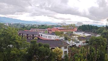 Blick auf eine Stadt mit Gebäuden, umgeben von dichtem Grün und Bergen im Hintergrund.