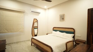 A bedroom with a bed, a ceiling fan, an air conditioner, a mirror, a bedside table, and a framed picture on the wall. - Angelo's farm (Amer)