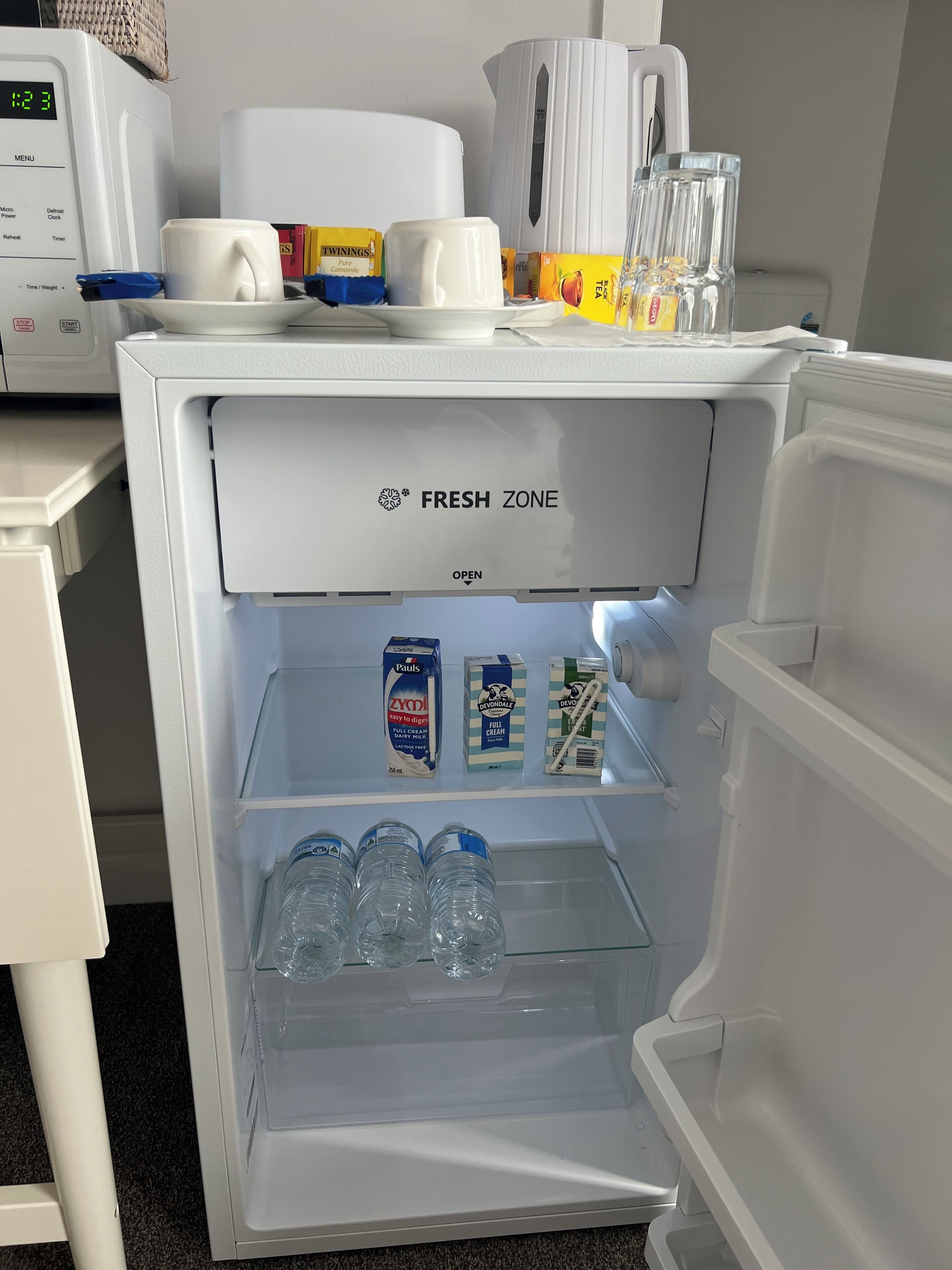 A refrigerator with a 'FRESH ZONE' label, containing milk cartons, a carton of 'Pauls' yogurt, and bottled water.