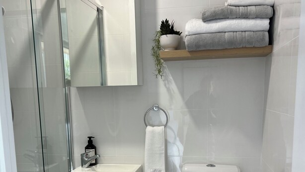 Une salle de bain moderne avec une douche à parois de verre, un lavabo blanc, des toilettes et une petite poubelle.