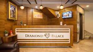 A reception desk with a wooden finish and the name "Diamond Palace" prominently displayed. There are two pendant lights above the desk, a framed picture on the wall, and a television mounted on the wall. - Diamond palace (bengalore)