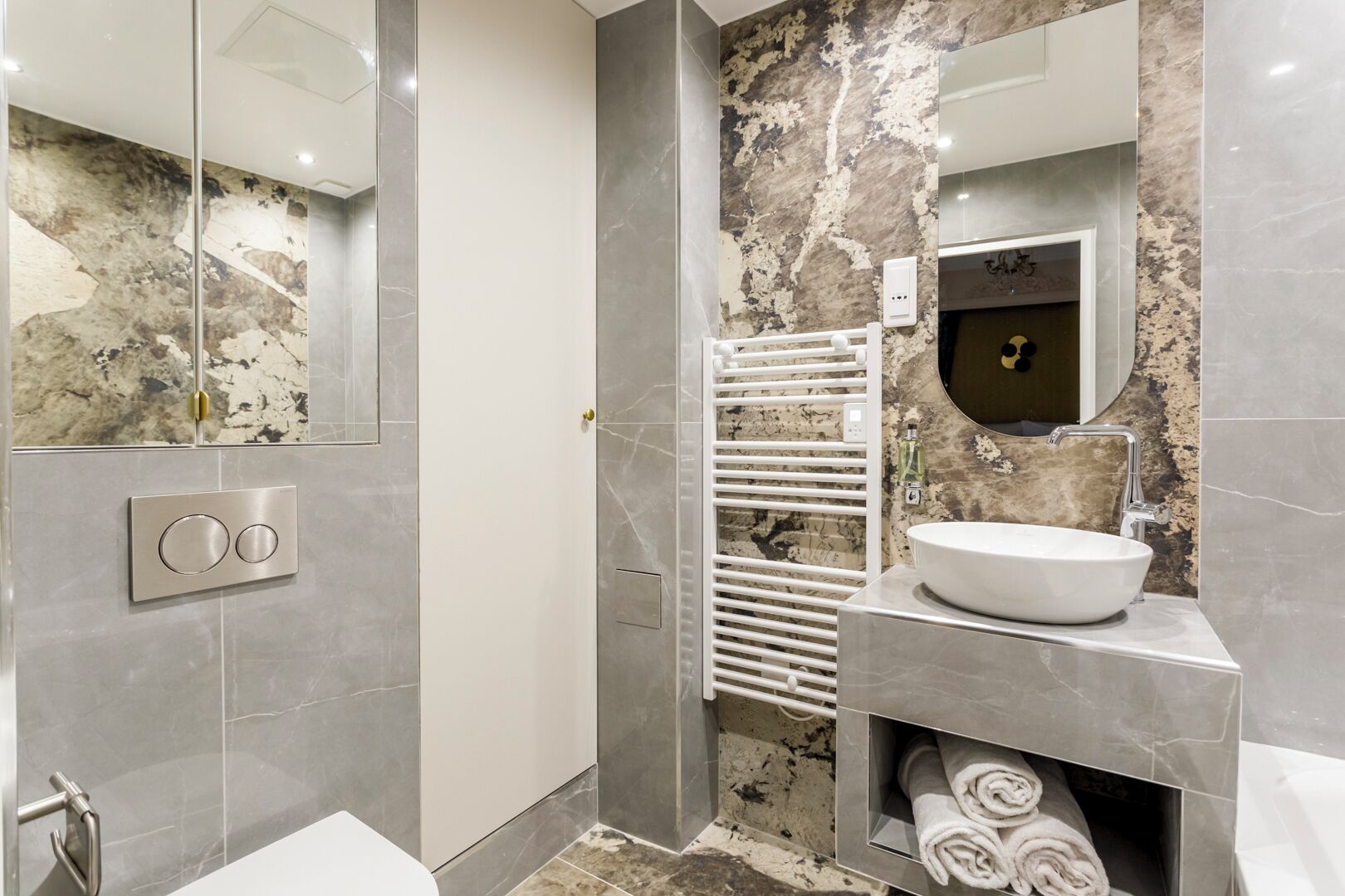 A modern bathroom with a marble sink, a towel rack, and a shower area.
