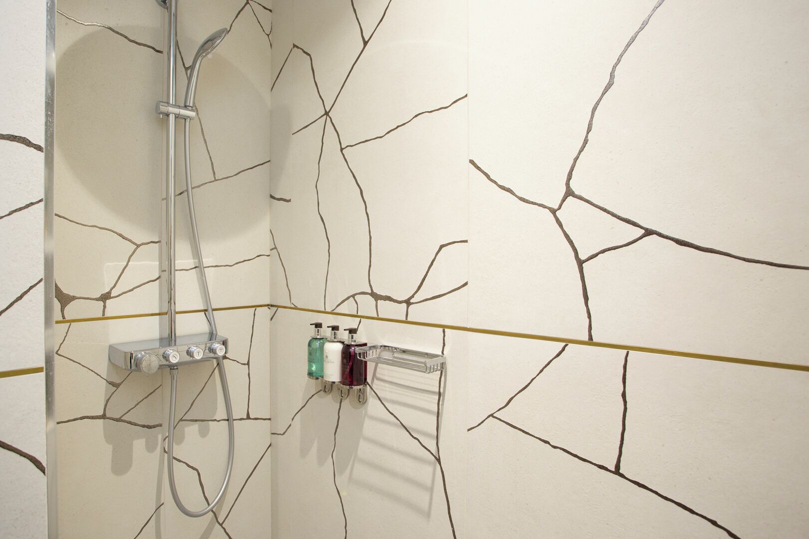 Une salle de bain avec un motif de fissures sur le mur, une douche et un distributeur de savon liquide.