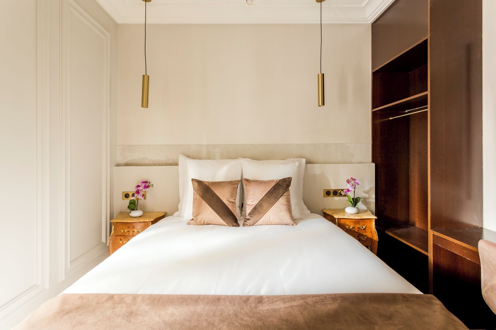 A neatly arranged bedroom with a large bed, two bedside tables, a wardrobe, and pendant lights.