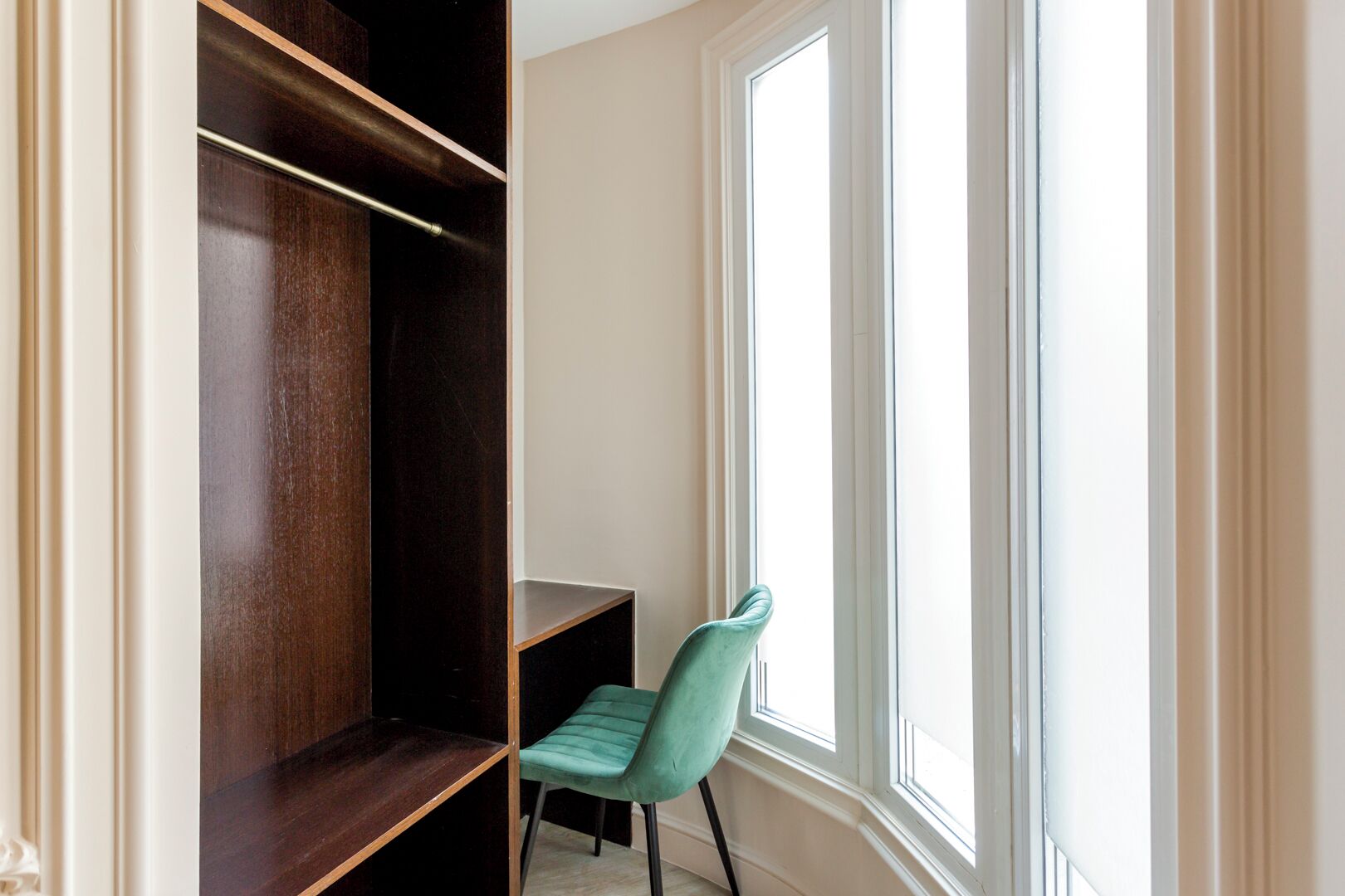 Une pièce avec une armoire en bois, un fauteuil de couleur turquoise et une fenêtre laissant entrer la lumière naturelle.