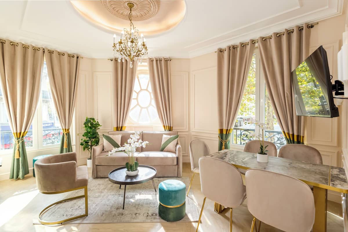 A spacious living room with a beige sofa, a round coffee table, and a dining area with a marble table and chairs.