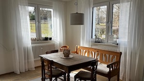 Un comedor con una mesa y sillas, una lámpara colgante y ventanas con cortinas.