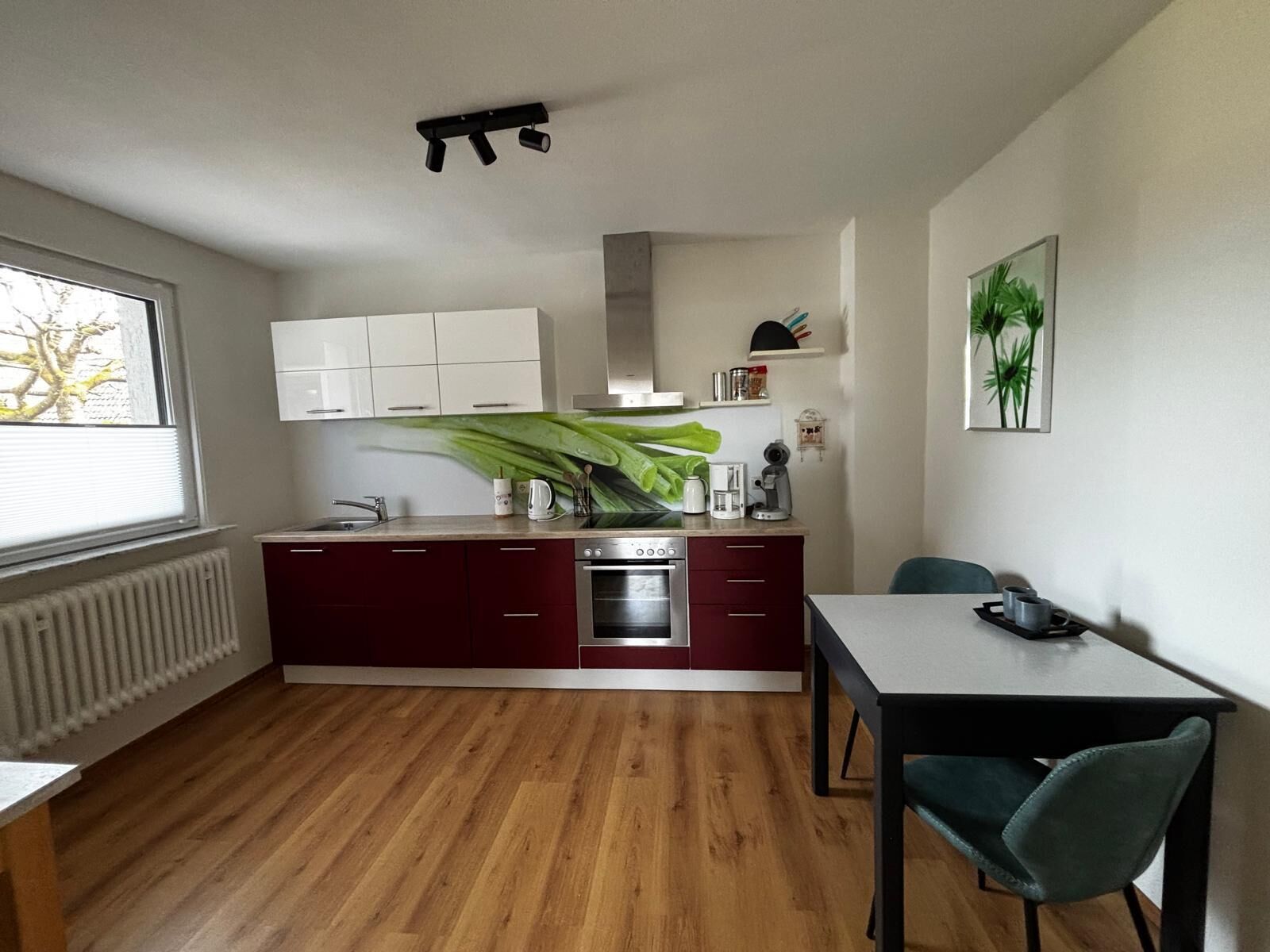 A compact kitchen with a central island, a dining table with chairs, and a window with blinds.