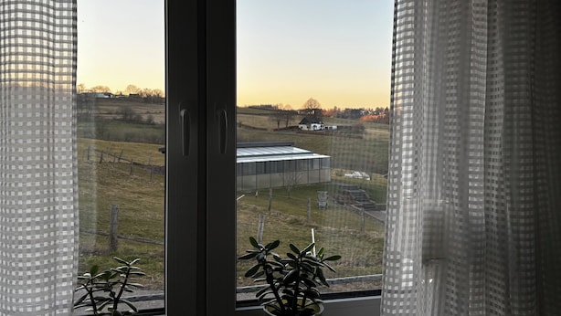 Una ventana con vistas a un paisaje rural, que incluye campos y un edificio distante.