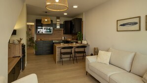 A modern kitchen with a central island, two bar stools, and a hanging light fixture.