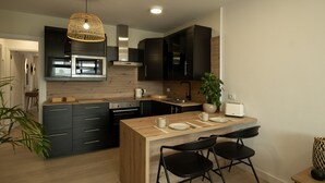 A modern kitchen with dark cabinetry, a wooden island, and black chairs.