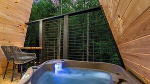 A hot tub with a wooden deck and a wicker chair. - Treehouse A-Frame, Sauna, Mini Golf, Fully Stocked (Sevierville)