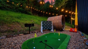 A miniature golf course with a green artificial turf, a wooden barrel, and a signboard. - Treehouse A-Frame, Sauna, Mini Golf, Fully Stocked (Sevierville)