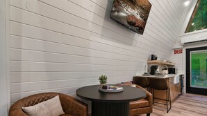 A modern interior with a round table, leather chairs, a mounted TV, and a kitchen area. - Treehouse A-Frame, Sauna, Mini Golf, Fully Stocked (Sevierville)
