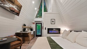 A modern hotel room with a bed, a desk, a chair, and a fireplace. - Treehouse A-Frame, Sauna, Mini Golf, Fully Stocked (Sevierville)