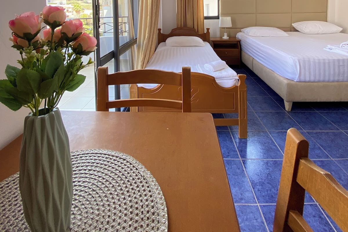 A hotel room with two beds, a wooden table with a vase of flowers, and a view of the city through large windows.