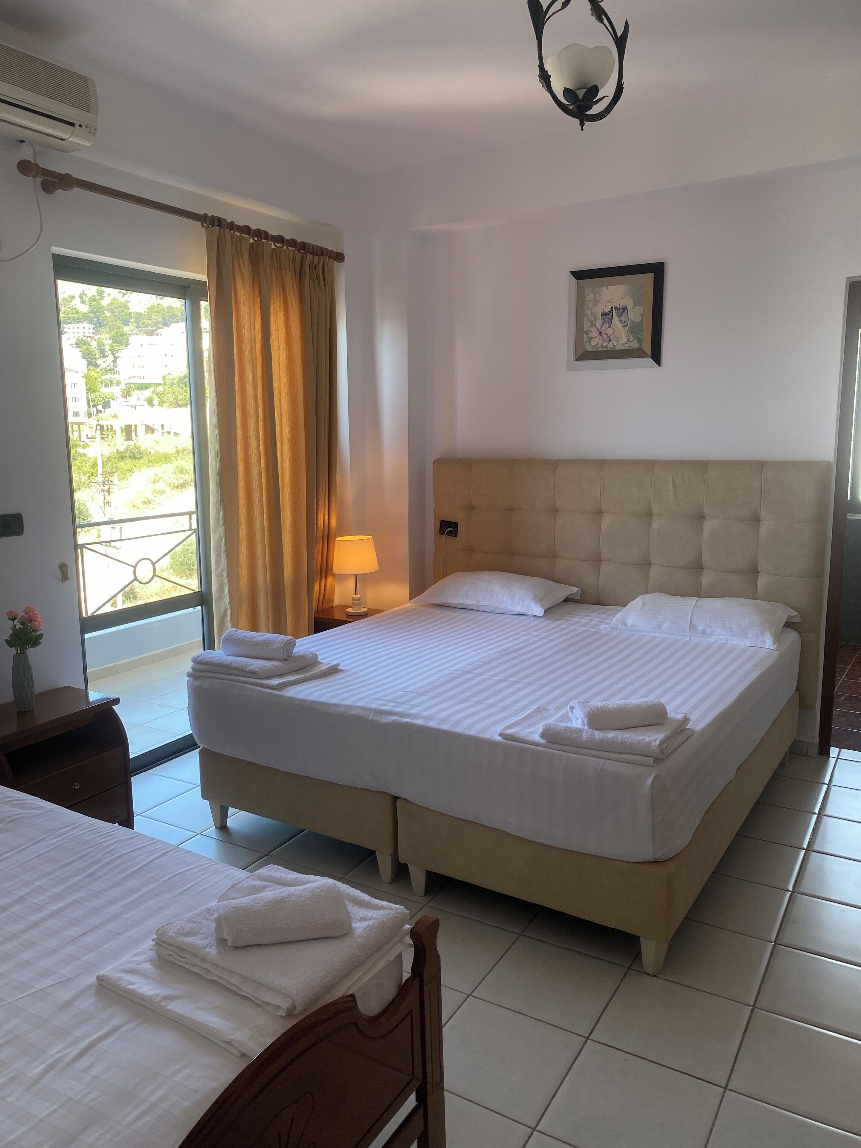 A hotel room with a large bed, a bedside table, a lamp, and a view of the outside.