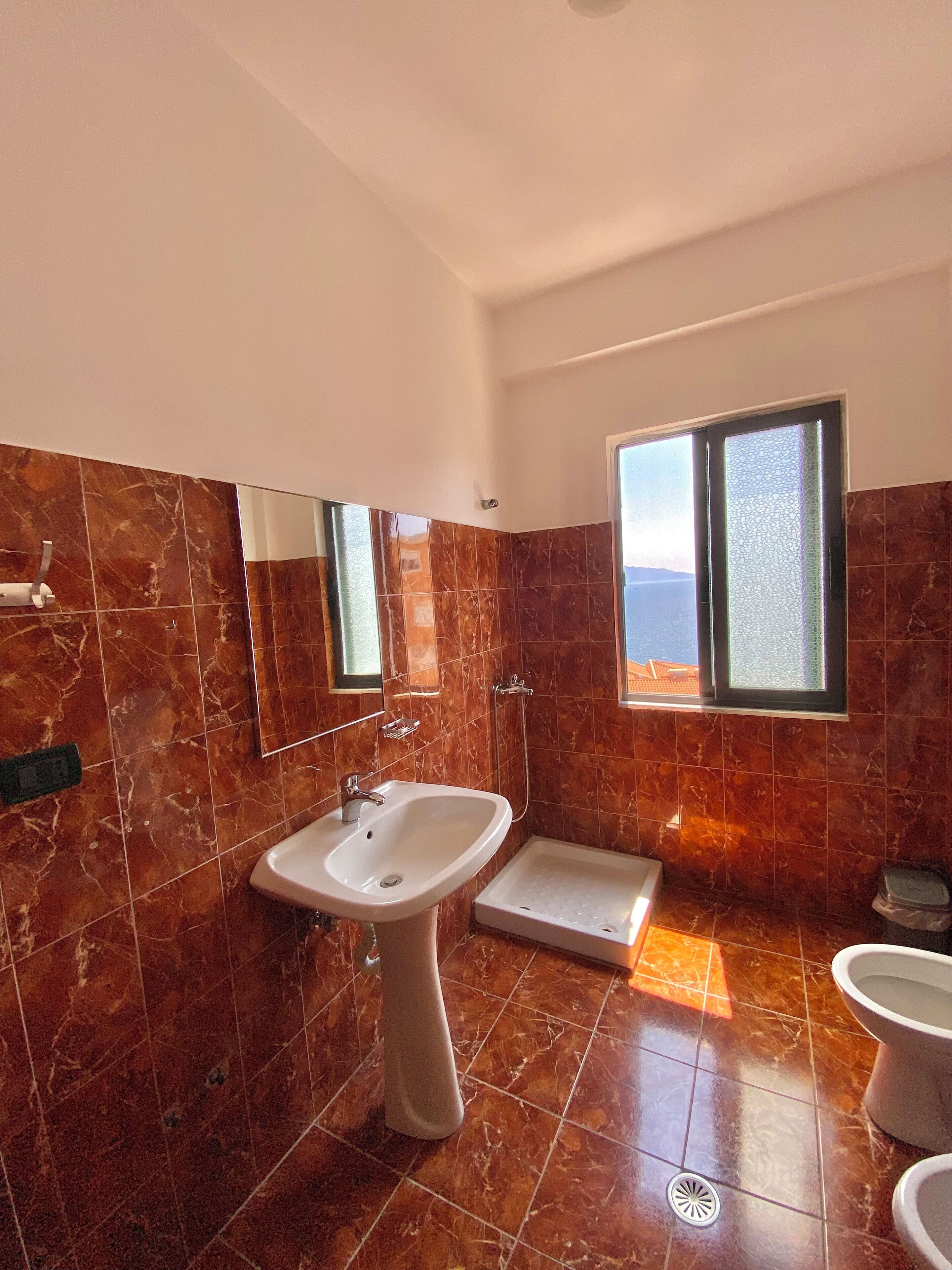 Un baño moderno con pared de azulejos de mármol, un lavamanos blanco, una ducha y un inodoro.