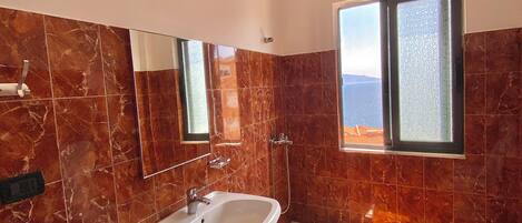 Un baño moderno con pared de azulejos de mármol, un lavamanos blanco, una ducha y un inodoro.