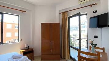 Habitación de hotel con cama, armario de madera, escritorio con silla, televisor y ventana con vista a edificios.