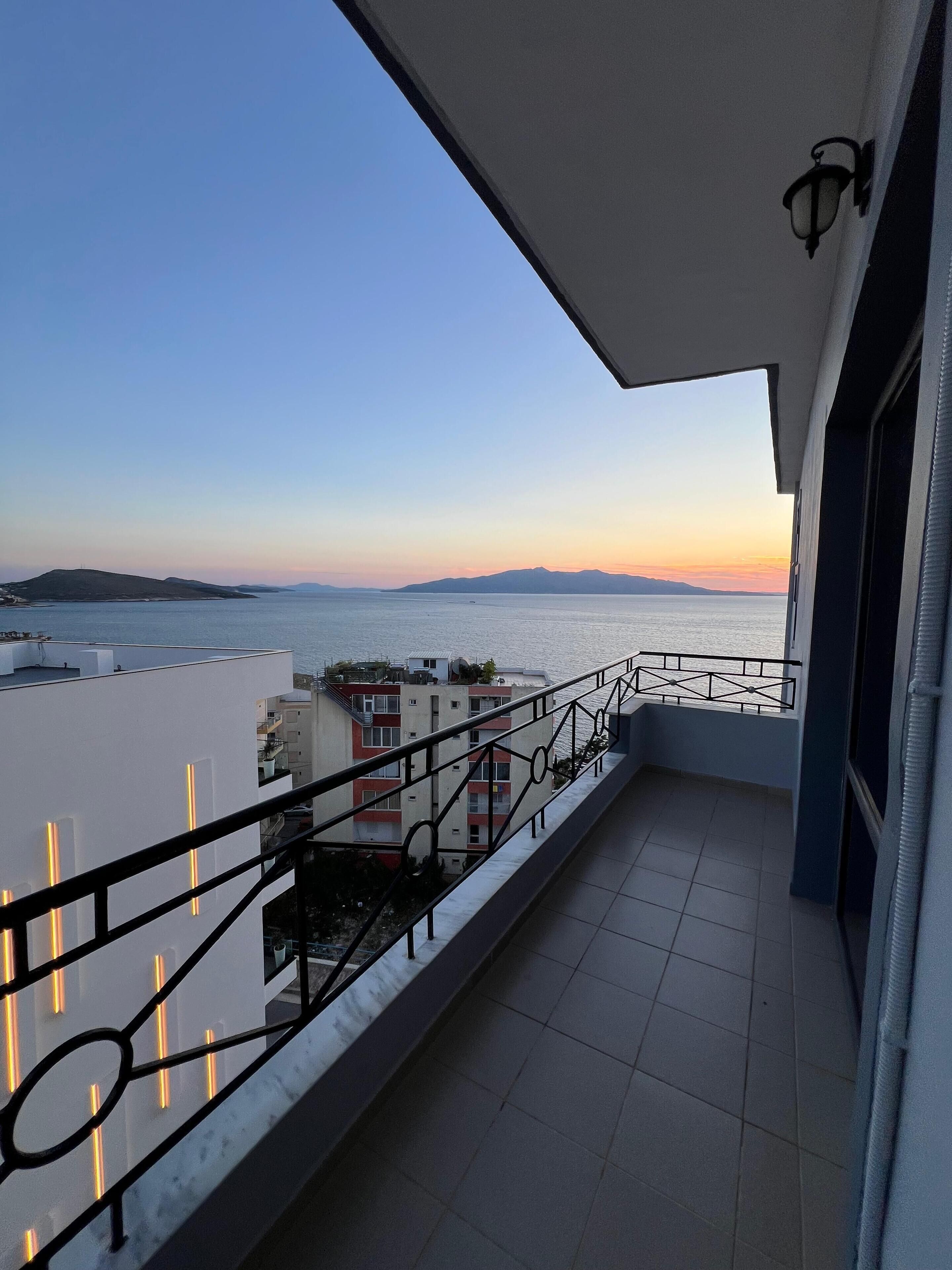 A balcony with a view of the sea and distant mountains during sunset.