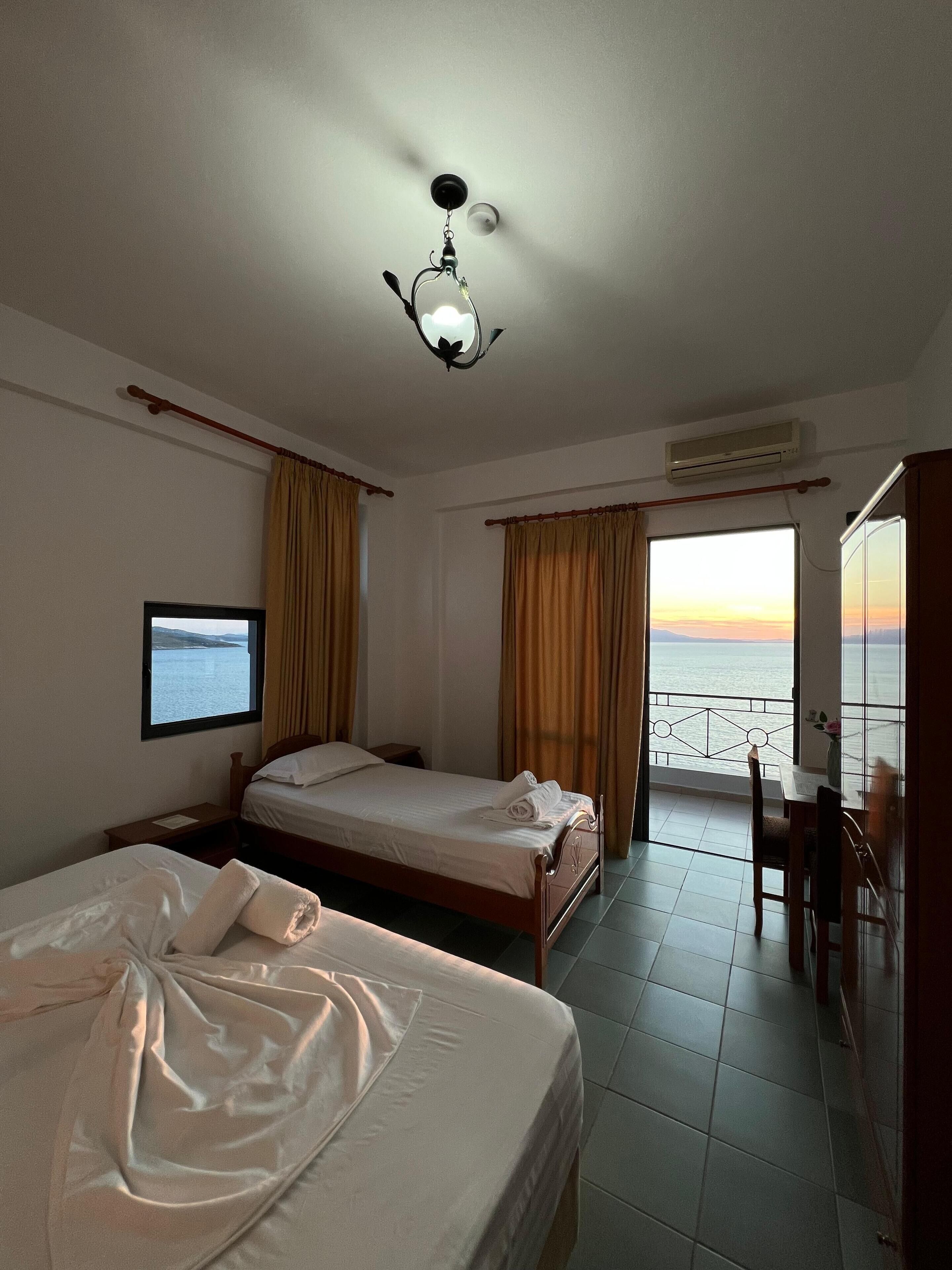 Camera d'albergo con due letti, una televisione, un balcone vista mare e un condizionatore.