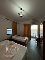 Camera d'albergo con due letti, una televisione, un balcone vista mare e un condizionatore.