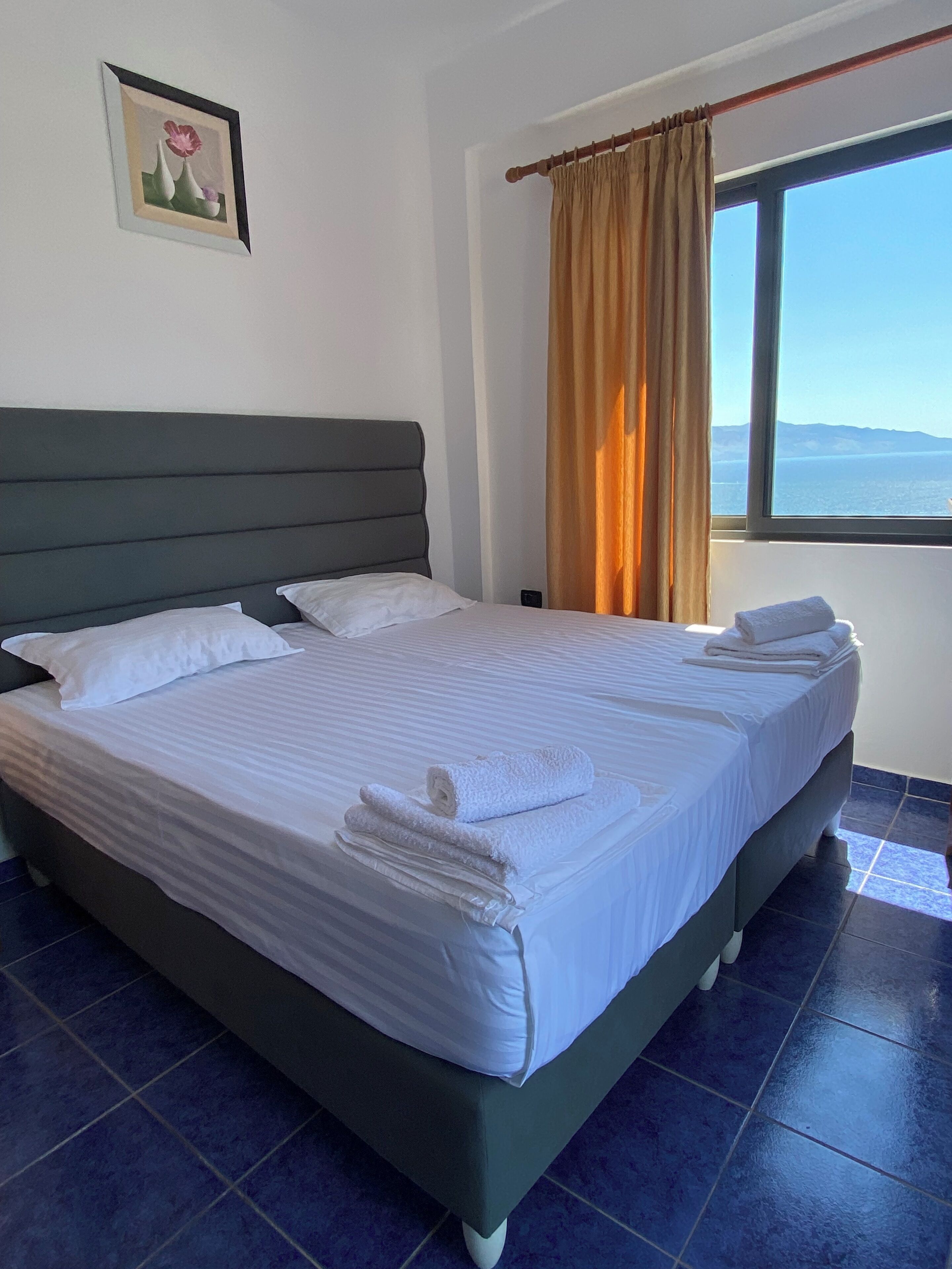 A neatly made bed with white linens and towels, a dark headboard, and a window with curtains.