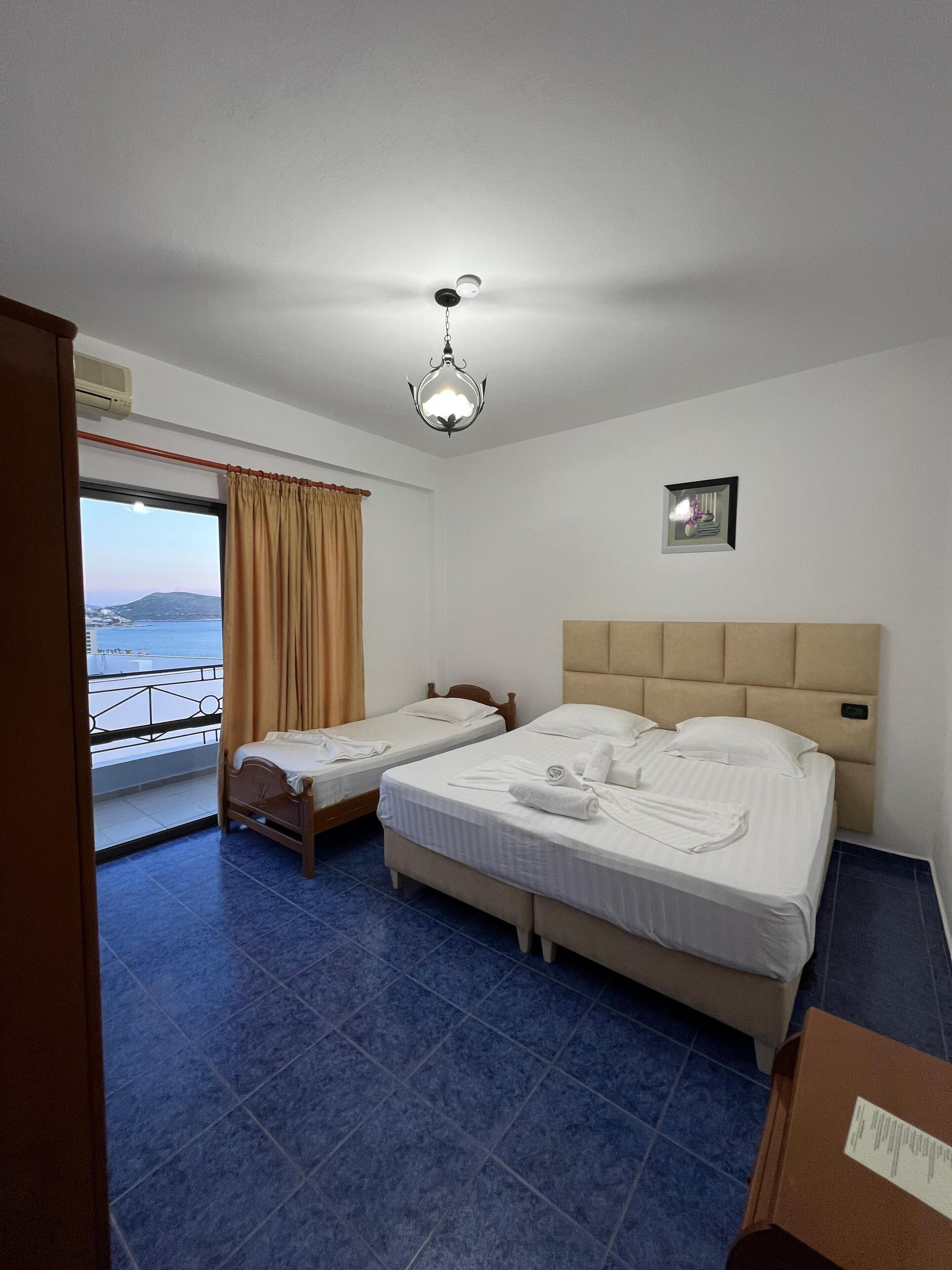 A hotel room with two single beds, a large window with a view, a ceiling light, and a small picture on the wall.