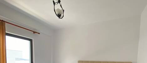 Habitación de hotel con dos camas individuales, un ventanal grande con cortinas, cabecero de madera y una lámpara colgante.