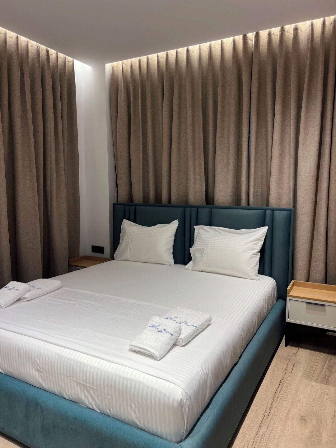 Habitación de hotel con una cama grande, dos almohadas, una mesita de noche y piso de madera.