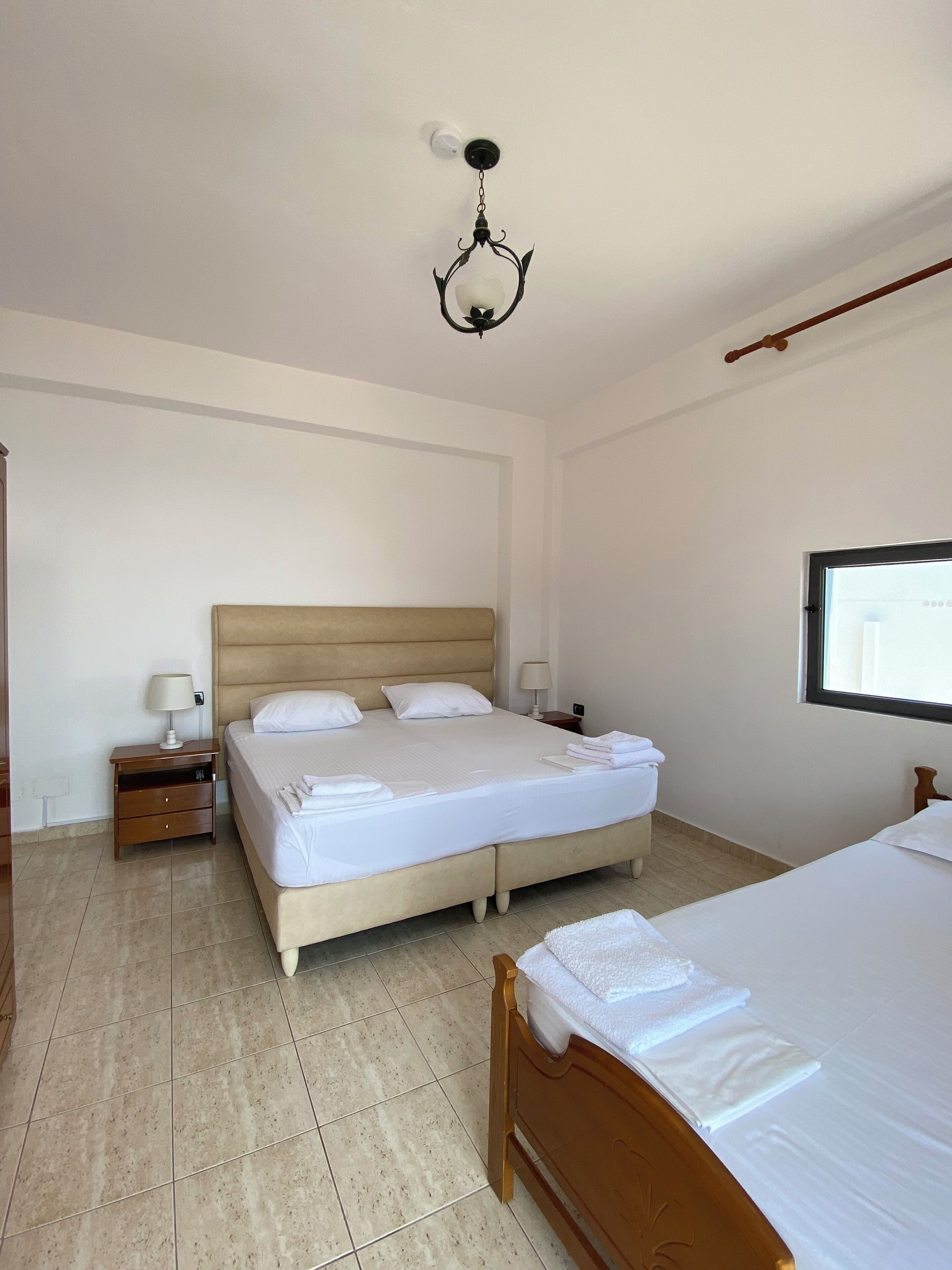 Una habitación de hotel con una cama grande, una mesita de noche, una lámpara, un candelabro en el techo y una ventana.