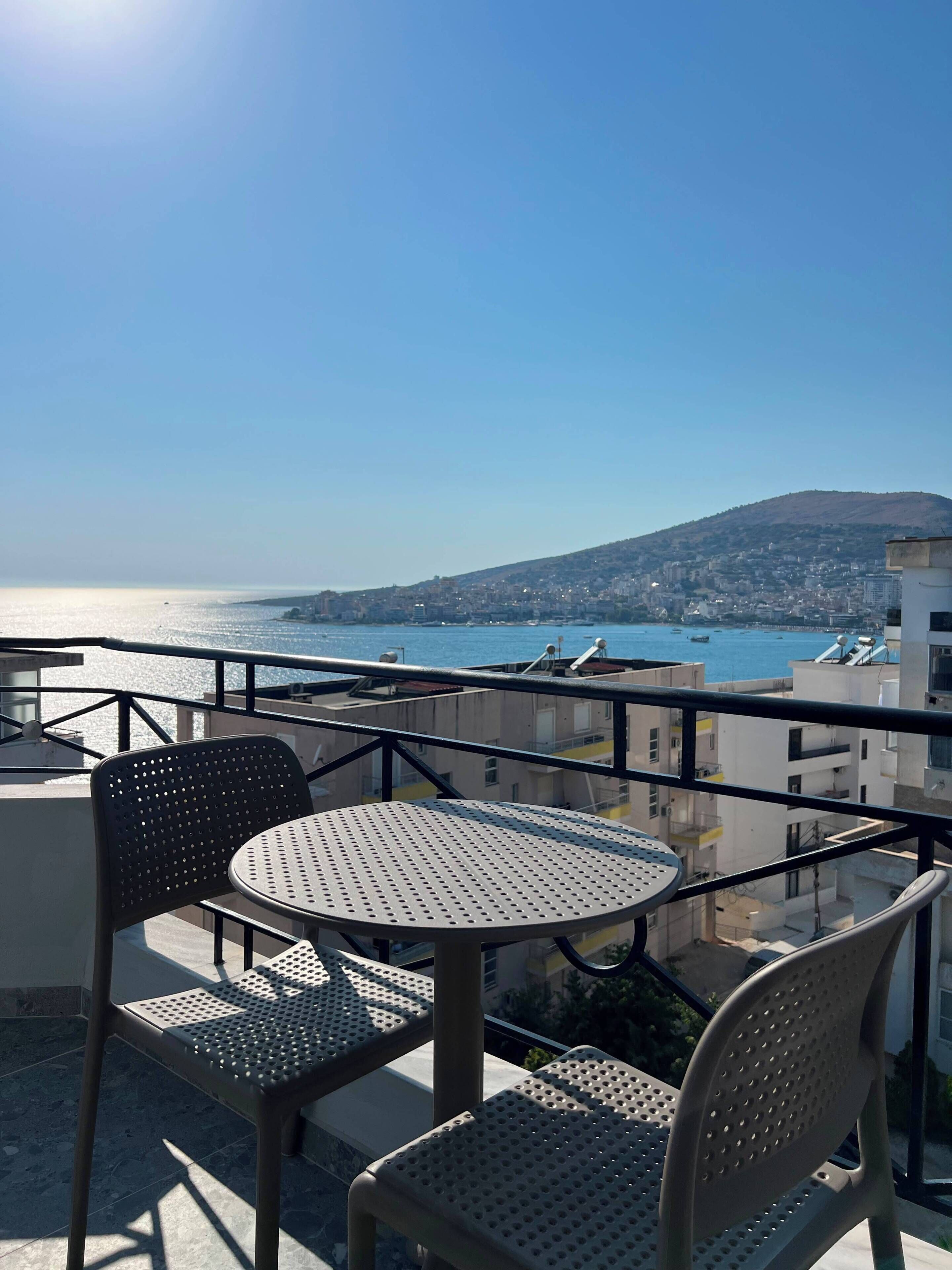 A balcony with a table and chairs overlooking a coastal cityscape.