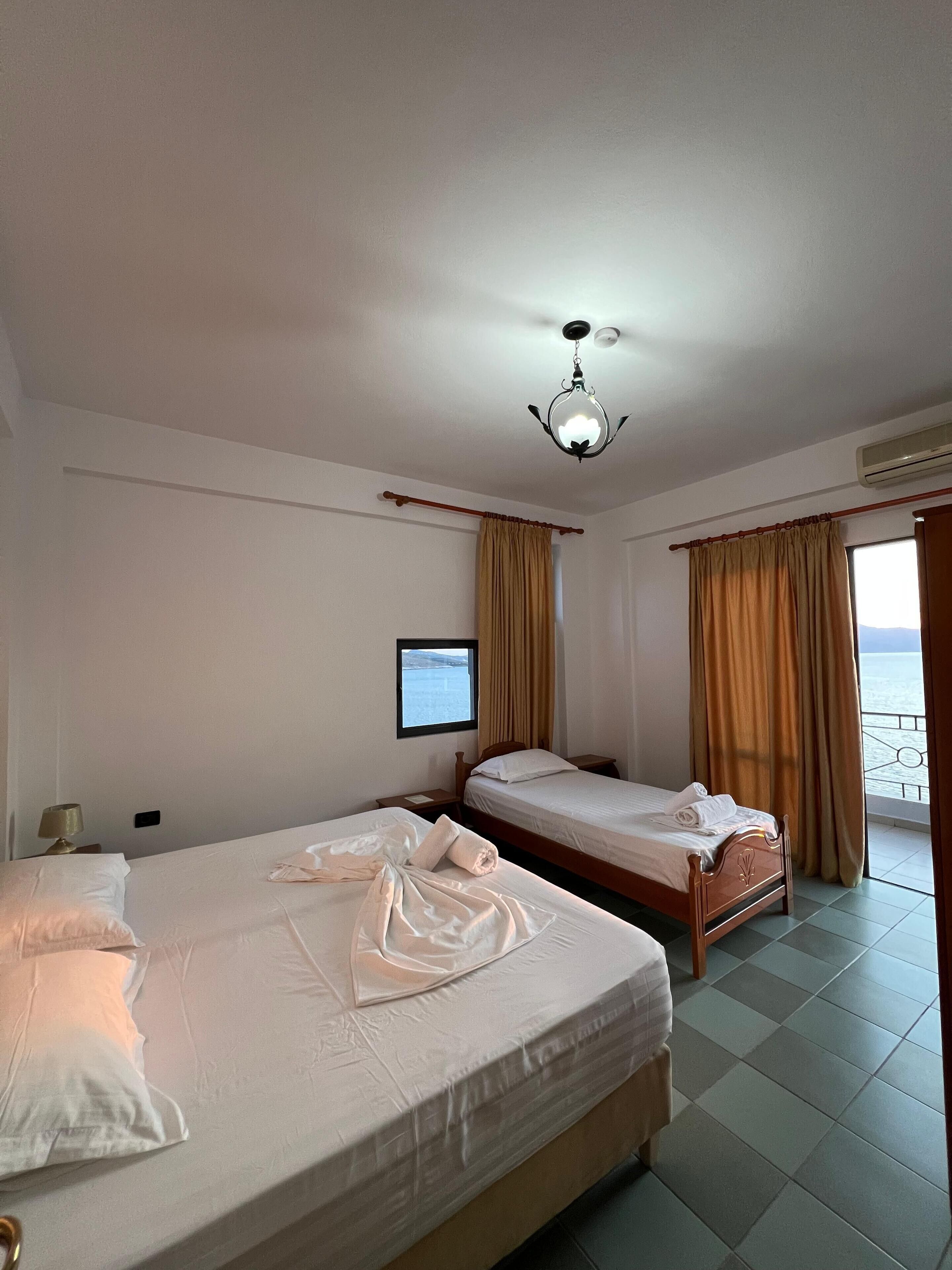 A hotel room with two beds, a ceiling light, an air conditioner, and a window with curtains.