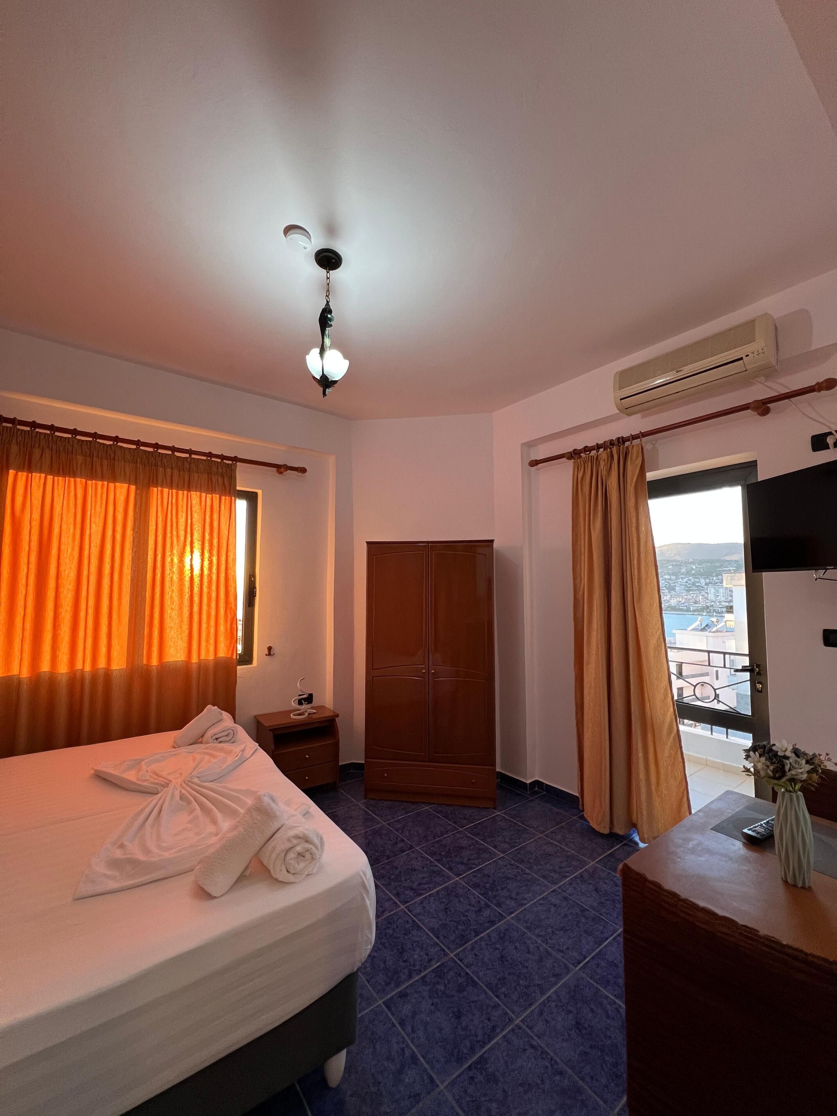 A hotel room with a bed, a wardrobe, a small table with a vase, and a view through a door.