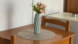 A wooden table with a woven placemat, a vase with pink flowers, and a television mounted on the wall. - Blue Waves Hotel & Suites (Sarandë)