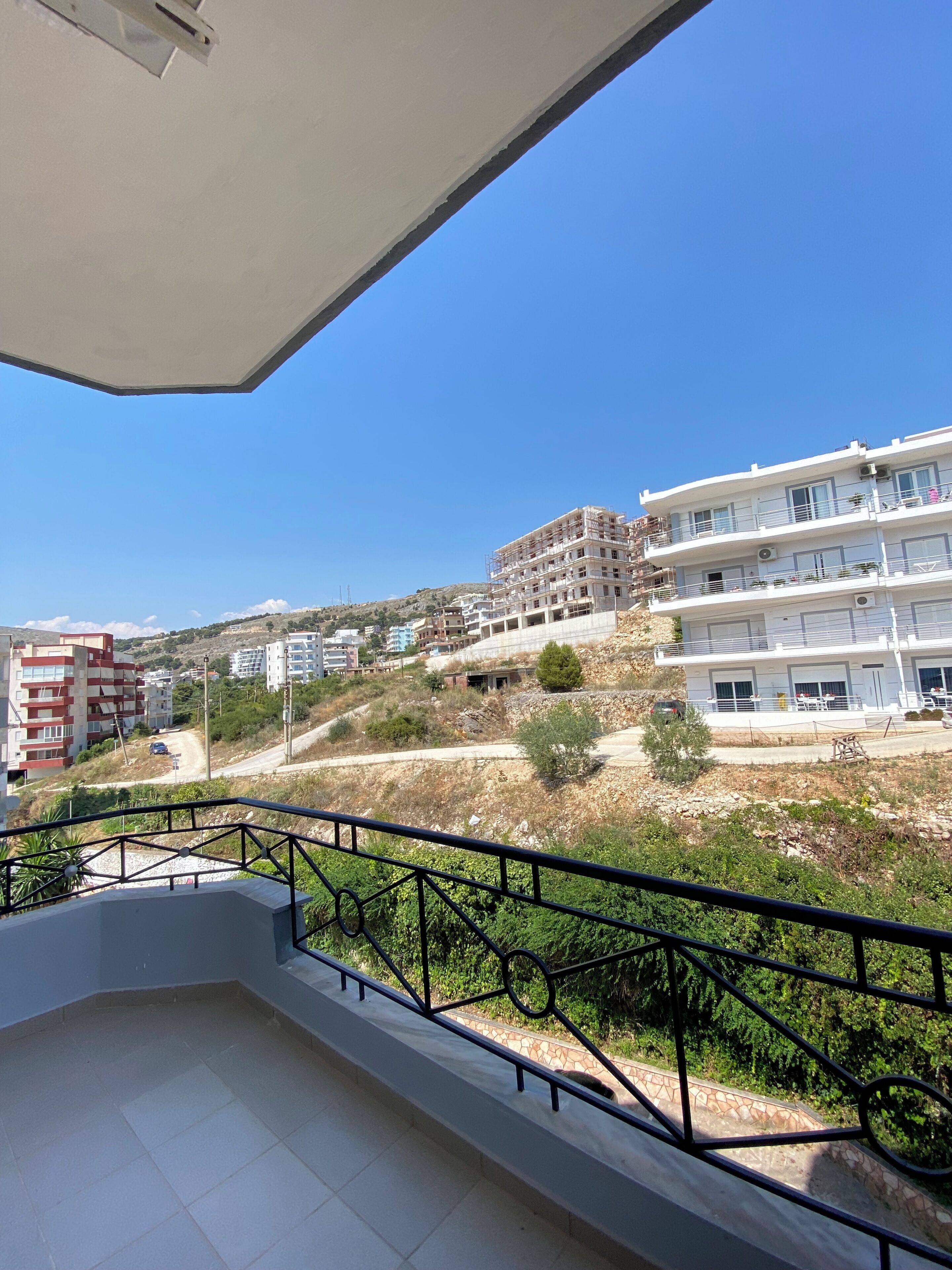 A balcony with a view of a hillside with buildings, a dirt path, and some greenery.