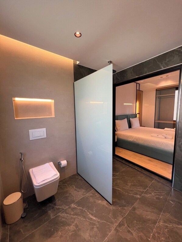 Ett modernt hotellrum med en stor säng, ett separat badrum och en skjutdörr som leder ut till en balkong.