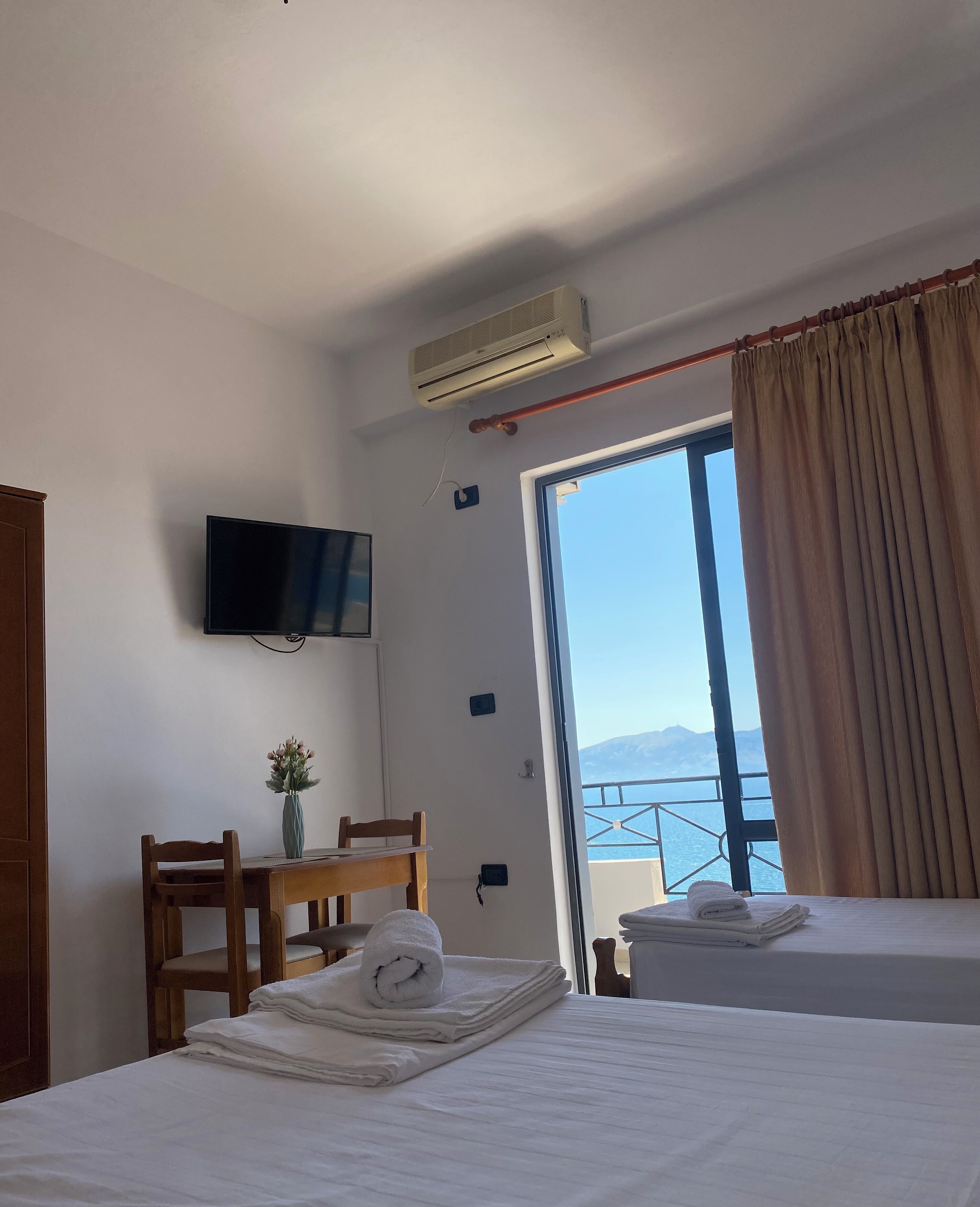 A hotel room with a bed, a desk with a chair, a television, and a large window with curtains.