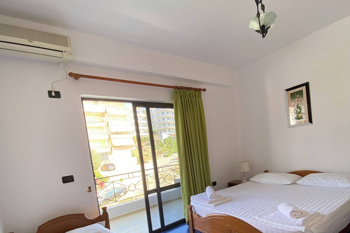A hotel room with two wooden beds, a sliding glass door to a balcony, and a ceiling fan.