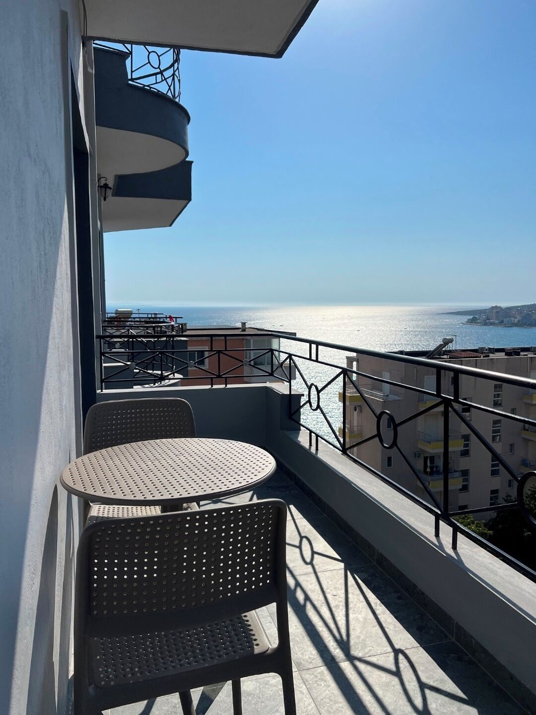 A balcony with a table and chairs, overlooking a body of water and buildings.