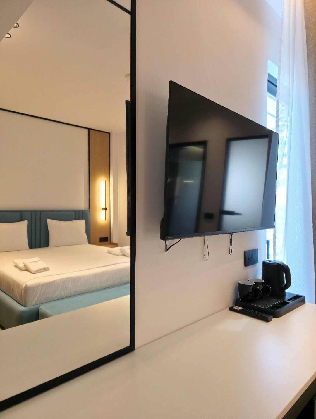 A hotel room with a bed, a flat-screen TV mounted on the wall, a coffee maker, and a bedside table.