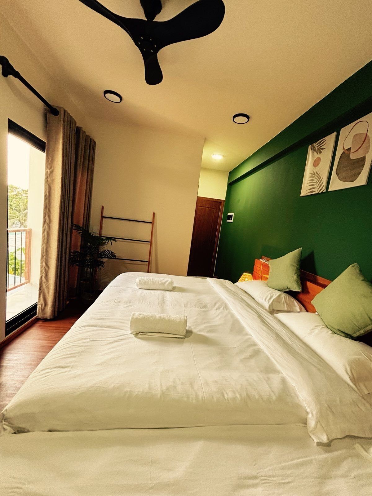 A hotel room with a large bed, two pillows, a ceiling fan, and a window with curtains.