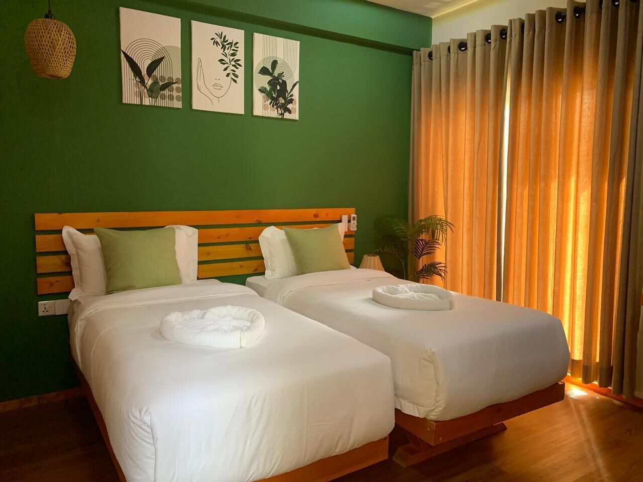 A hotel room with two beds, green walls, and a large window with curtains.