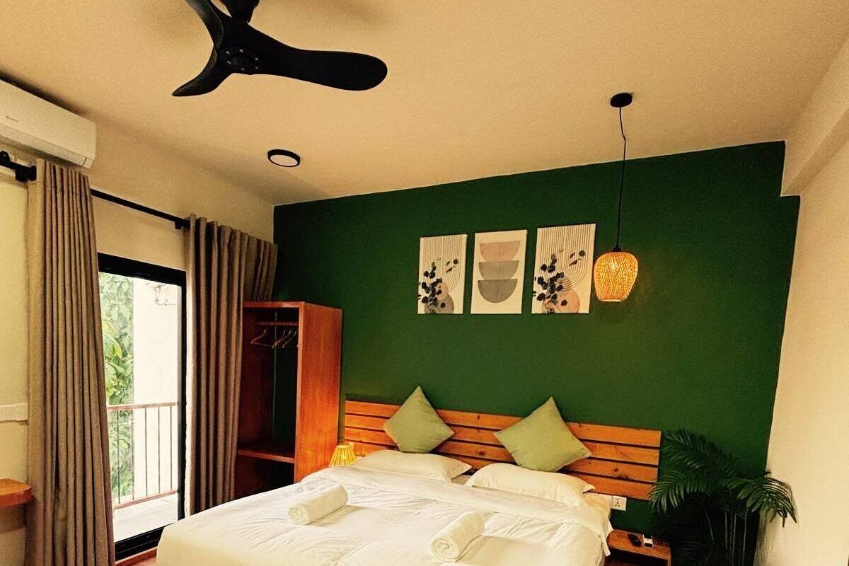 A bedroom with a bed, a ceiling fan, a wardrobe, a nightstand, and a potted plant.