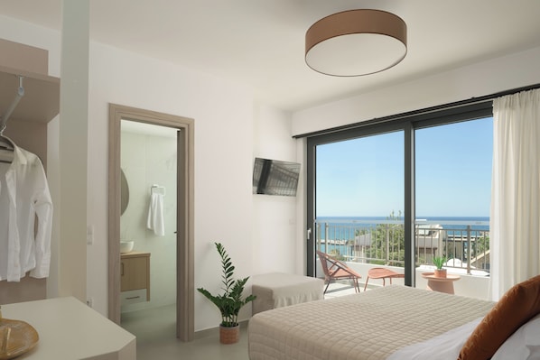 A modern hotel room with a large bed, a bathroom with a mirror, and a balcony with a view of the ocean.